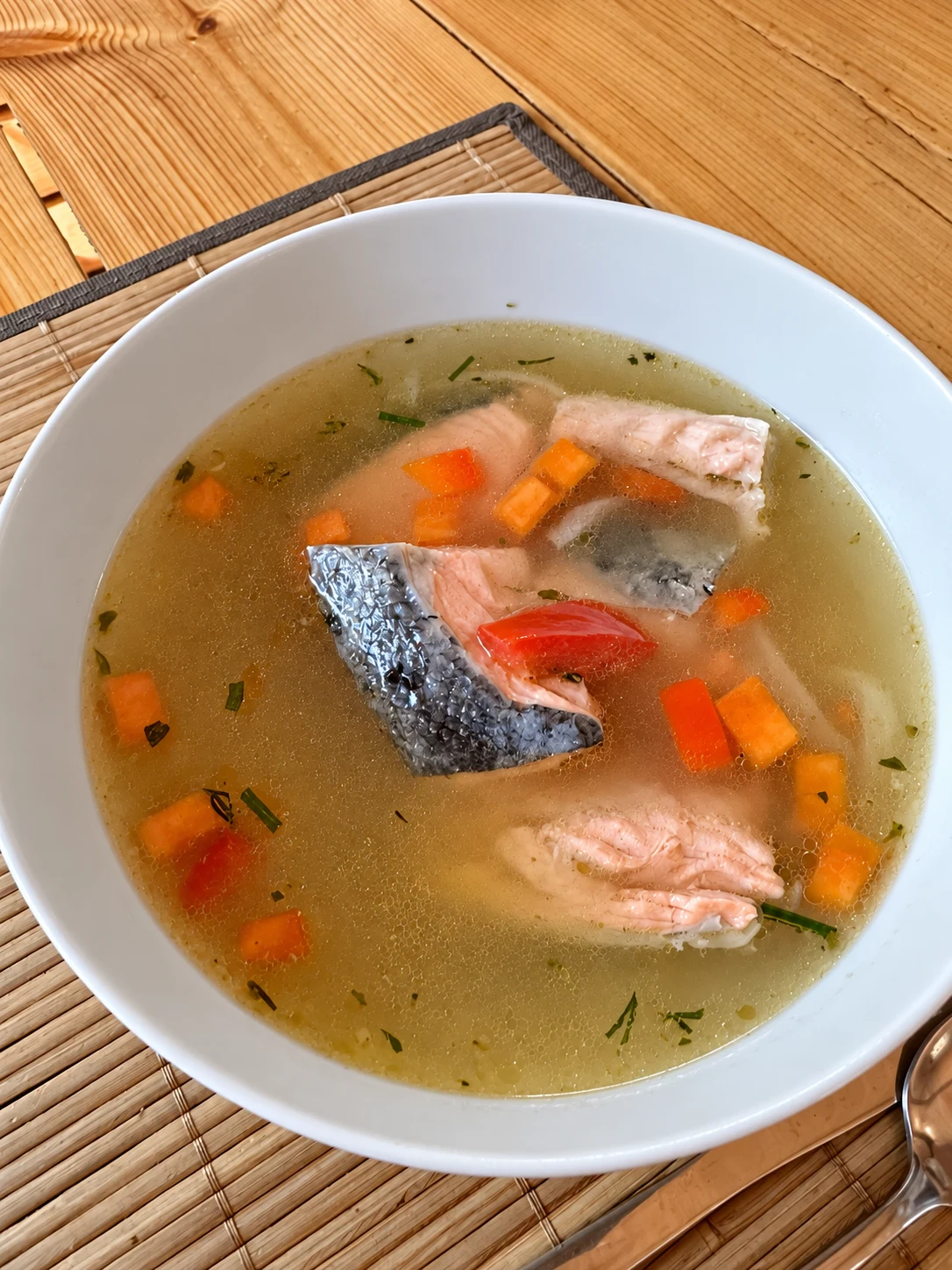 Тарелка ухи с кусочками рыбы и овощами на деревянном столе базы «Пана»